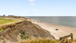 Un paysage côtier avec une plage de sable, une clôture en bois et une falaise couverte de végétation.