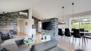 Ein modernes Wohnzimmer mit Kamin aus Naturstein, einem Flachbildfernseher und einem Essbereich mit schwarzen Stühlen.