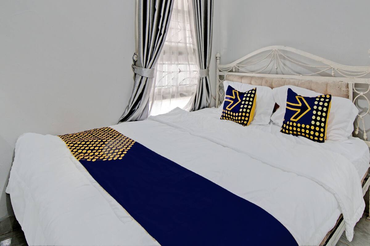 Een net opgemaakt bed met een wit en marineblauwe sprei, twee kussens met geometrische patronen, en een wit hoofdbord.