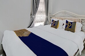A neatly made bed with a white and navy blue bedspread, two pillows with geometric patterns, and a white headboard. - Hotel O Teguh Homestay Syariah (Pekanbaru)