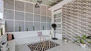 A modern living room with a white sofa, a patterned rug, and a large window with a view of cacti. - Hotel O Teguh Homestay Syariah (Pekanbaru)