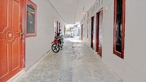 A narrow corridor with a motorcycle parked on the left, leading to a building with multiple doors and windows. - Hotel O Teguh Homestay Syariah (Pekanbaru)