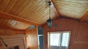Interno in legno con soffitto alto, una porta centrale e una finestra con persiane a forma di cuore.