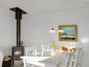 A room with a white table, chairs, a painting, a bottle, and a fruit bowl.