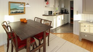 Ein Essbereich mit einem Holztisch und rot gepolsterten Stühlen, eine Küche mit weißen Schränken und einem Bild an der Wand.