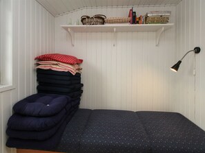 Una habitación pequeña con una cama, un estante con libros y objetos decorativos, y una lámpara de pared.