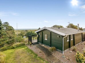 A single-story cabin with a sloped roof, a small porch, and a view of the ocean.