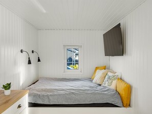 A bedroom with a bed, a window, a plant, and a TV mounted on the wall.