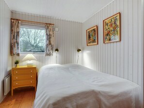 Un dormitorio con una cama, una mesita de noche con lámpara, un aparador y dos cuadros en la pared.