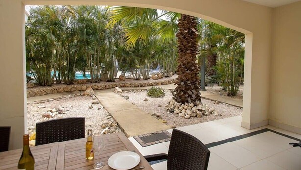 A patio with a table, chairs, and a bottle of wine. There is a palm tree and a view of the beach. - Trupial C3 Relax & Dive Resort Bonaire Village (Kralendijk)