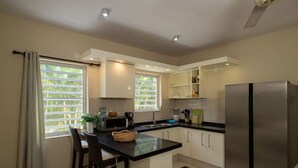 A modern kitchen with a central island, bar stools, a refrigerator, and built-in shelves. - Trupial C3 Relax & Dive Resort Bonaire Village (Kralendijk)
