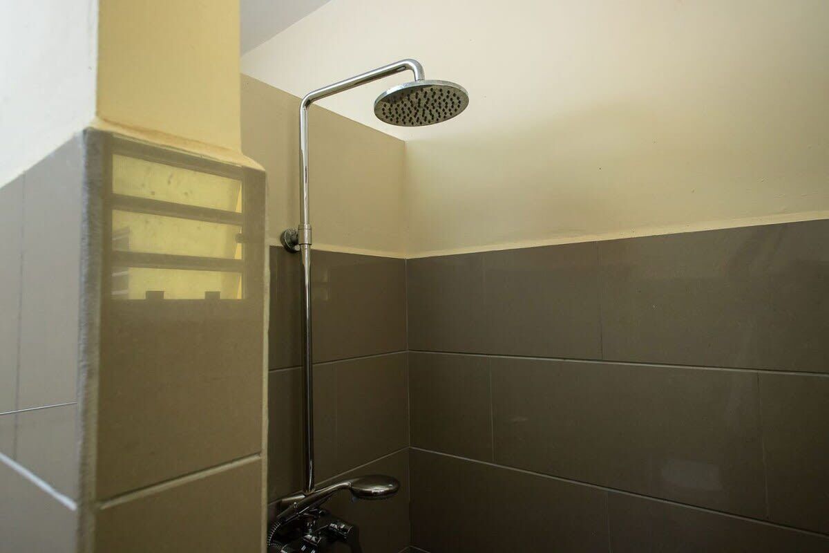 Zona de ducha con cabezal de ducha de mano, lavabo en esquina y paredes con azulejos.