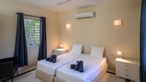 A hotel room with two beds, a desk, a chair, a ceiling fan, an air conditioner, and a window with curtains. - Trupial D3 Relax & Dive Resort Bonaire Village (Kralendijk)