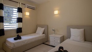 Habitació d'hotel amb dos llits individuals, una petita taula de nit amb una làmpada, un aparell d'aire condicionat i una finestra amb cortines.