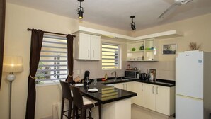 A compact kitchen with white cabinets, a black countertop island, a microwave, a refrigerator, and a window with blinds. - Trupial G3 Relax & Dive Resort Bonaire Village (Kralendijk)