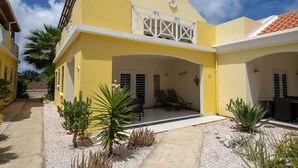 A yellow building with a covered patio area, outdoor seating, and a small garden with cacti. - Trupial G3 Relax & Dive Resort Bonaire Village (Kralendijk)
