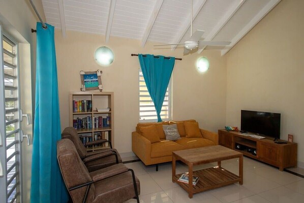 A living room with a sofa, chairs, a coffee table, a TV, and a bookshelf. - Prikichi C2 Relax & Dive Resort Bonaire Village (Kralendijk)