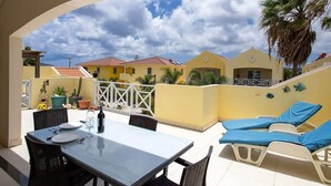 A patio with a table and chairs, a pool area with lounge chairs, and a view of neighboring buildings.
