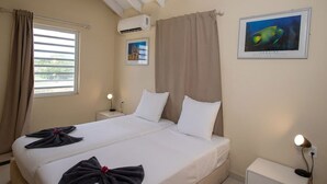 Une chambre d’hôtel comprenant un lit, deux tables de chevet, un appareil de climatisation, une fenêtre avec des rideaux et un tableau encadré au mur.