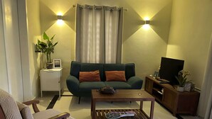 A living room with a green sofa, a wooden coffee table, a wooden side table with a plant, and a television on a wooden stand. - Caracara I2 Relax & Dive Resort Bonaire Village (Kralendijk)