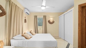 Un dormitorio con cama, cortinas, aire acondicionado, ventilador de techo, lámpara de pared y puerta corredera.