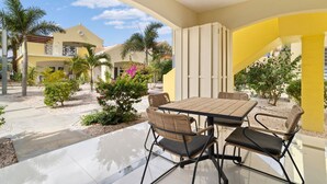 Un patio exterior con una mesa y sillas, rodeado por un jardín con diversas plantas y vistas a edificios vecinos.