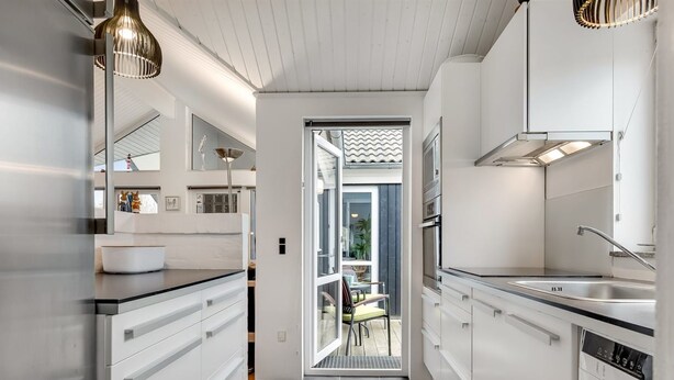 A modern kitchen with white cabinetry, a black countertop, and a view into an adjacent dining area.