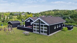 A modern house with a large patio, a swing set, and a view of a forested area.