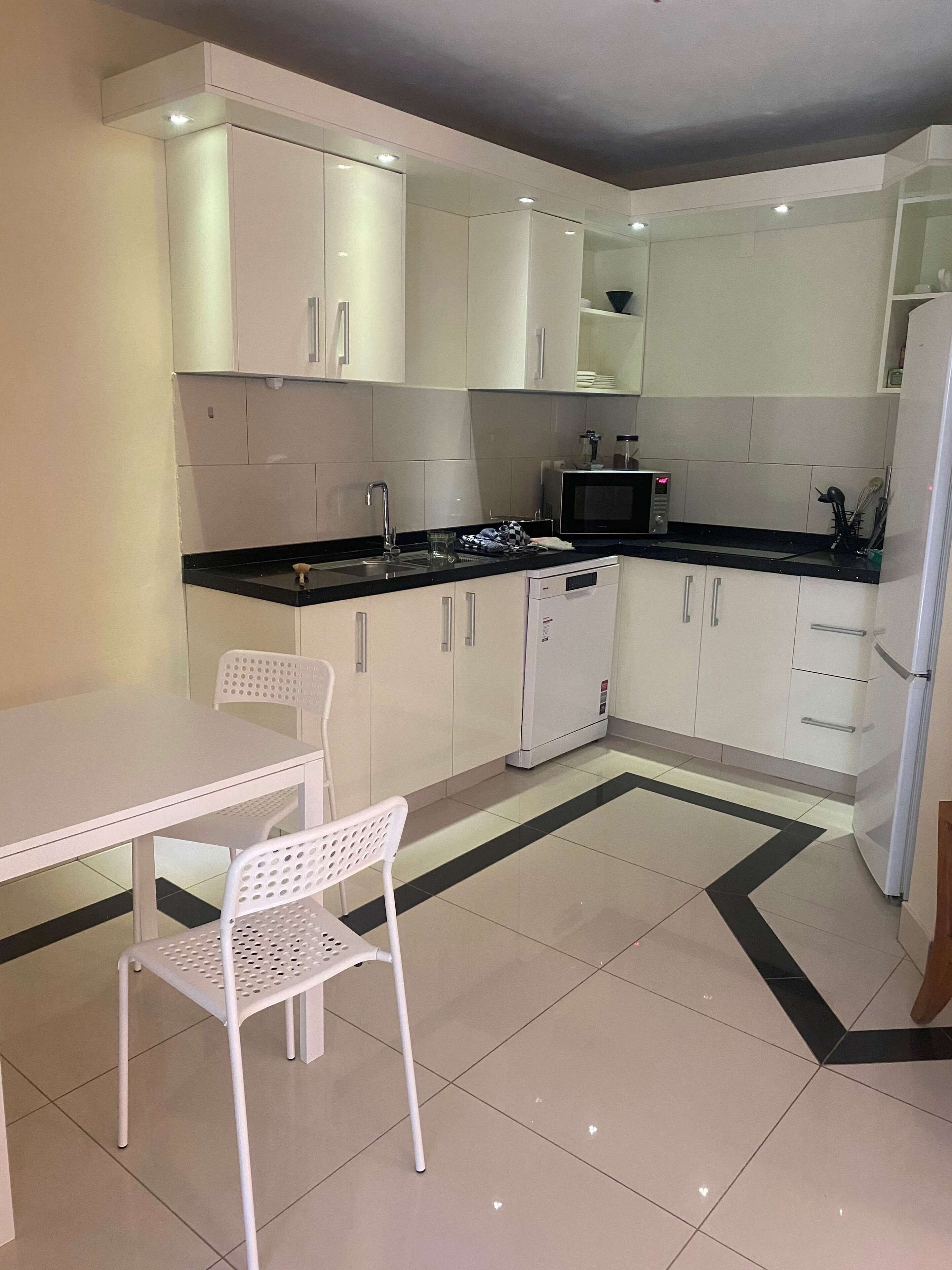 Una cocina compacta con armarios blancos, encimera negra, microondas y un refrigerador pequeño.