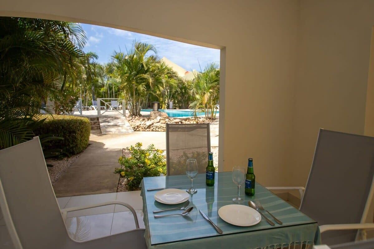 Mesa de comedor lista para dos personas, con vista a una piscina y palmeras.