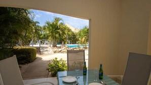Mesa de comedor lista para dos personas, con vista a una piscina y palmeras.