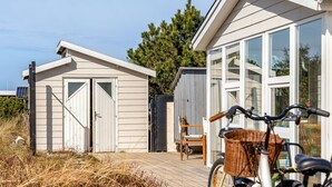 A wooden deck with a bicycle and a chair, a shed, and a house with large windows.