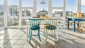 A sunroom with a large window, a table, chairs, and a hanging light fixture.
