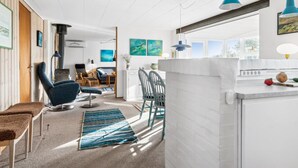 A modern kitchen with white cabinetry, a dining area with blue chairs, and a view of the outdoors through a large window.