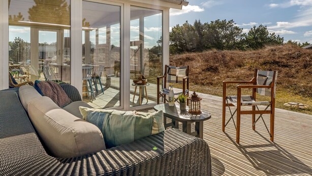 A covered outdoor seating area with a sofa, chairs, and a table, overlooking a natural landscape.