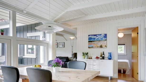 Une cuisine moderne avec une table et des chaises en bois, un coin repas offrant une vue sur l’extérieur et un tableau accroché au mur.