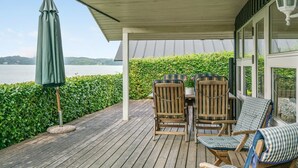 Un espace extérieur aménagé avec des chaises en bois et une table, protégé par un auvent et offrant une vue sur une étendue d’eau.