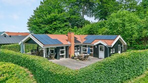 Un bâtiment doté d’un toit recouvert de panneaux solaires, d’un patio abrité avec des sièges d’extérieur et d’une cheminée en briques.