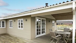 A covered outdoor deck with a wooden table and chairs, a covered patio area, and a view of a house in the background.
