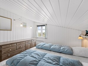 Une chambre à coucher avec un lit, une commode, une fenêtre et une lampe.