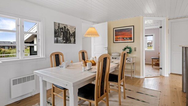 A dining area with a white table, wooden chairs, a lamp, and artwork on the walls.