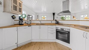 A modern kitchen with white cabinetry, wooden countertops, a built-in oven, and a large window.