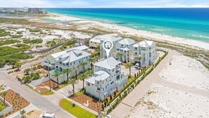 Un hotel costiero dall'architettura moderna, con diversi edifici dotati di balconi, posizionato vicino a una spiaggia con acque cristalline.