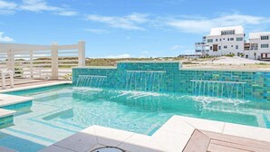 Una piscina con cascata, circondata da un recinto bianco e un edificio moderno sullo sfondo.