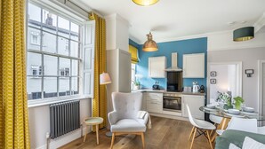 A modern kitchen with a blue accent wall, a dining area with a glass table, and a living room with a sofa and armchair. - A family retreat that sleeps 4 guests in 2 bedrooms (York)