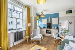 A modern kitchen with a blue accent wall, a dining area with a glass table, and a living room with a sofa and armchair. - A family retreat that sleeps 4 guests in 2 bedrooms (York)