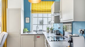 A modern kitchen with white cabinets, a sink, a window with a yellow patterned blind, and a coffee machine. - A family retreat that sleeps 4 guests in 2 bedrooms (York)