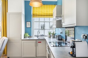 A modern kitchen with white cabinets, a sink, a window with a yellow patterned blind, and a coffee machine. - A family retreat that sleeps 4 guests in 2 bedrooms (York)