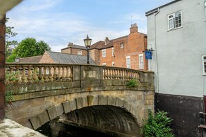A stone bridge with a lamp post, a white building with a blue sign, and a brick building in the background.