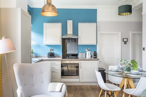 A modern kitchen with white cabinets, a blue accent wall, and a dining area with a glass table and white chairs. - A family retreat that sleeps 4 guests in 2 bedrooms (York)